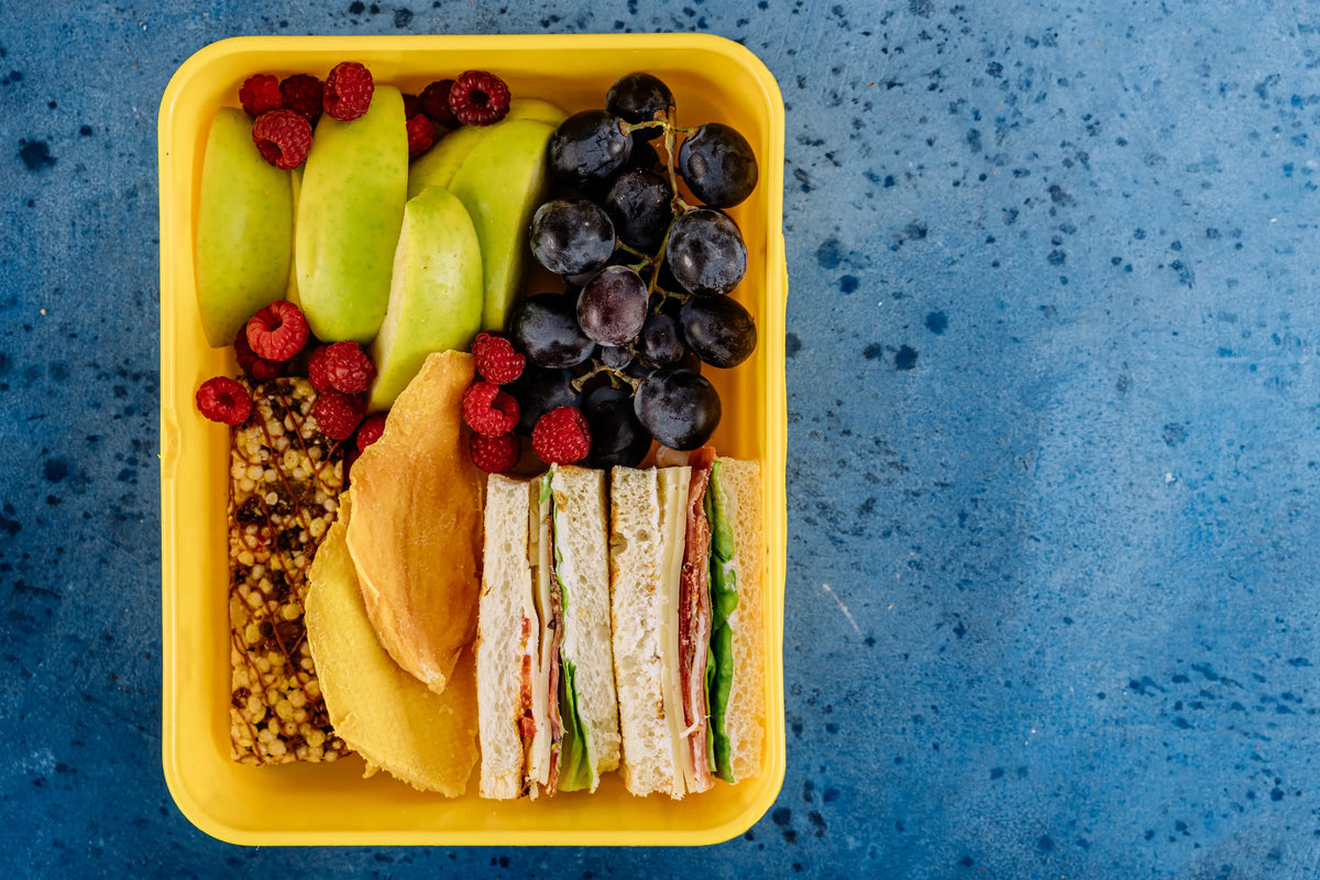 Bunte Kita-Brotdose mit belegten Broten, Apfelspalten, Trauben und Beeren – leckere Kita-Frühstück-Ideen für Kinder.