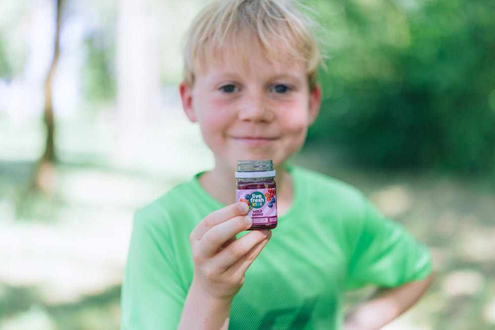 Junge hält einen geöffneten LiveFresh Kids Shot Waldbeere in die Kamera.