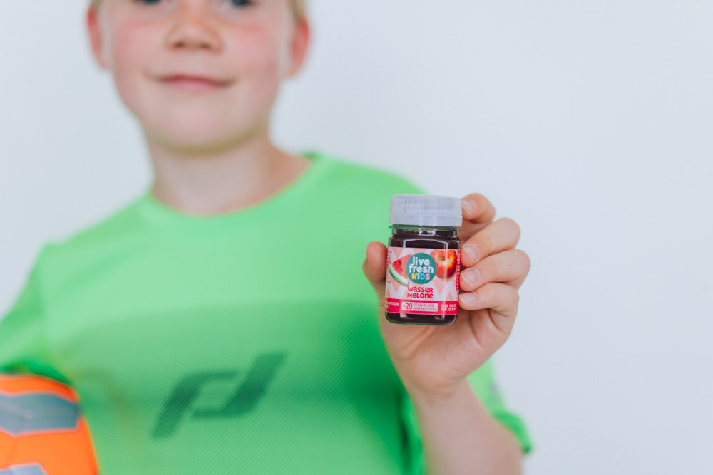 Junge im grünen Sportshirt hält einen LiveFresh Kids Shot Wassermelone.