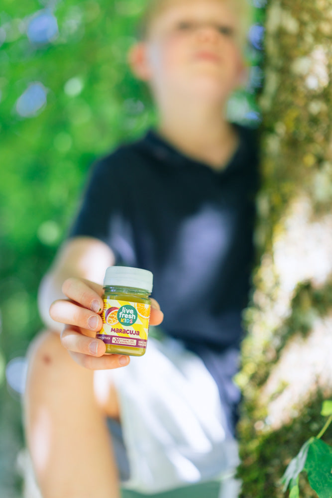 Kind sitzt an einem Baum und präsentiert einen LiveFresh Kids Shot Maracuja.